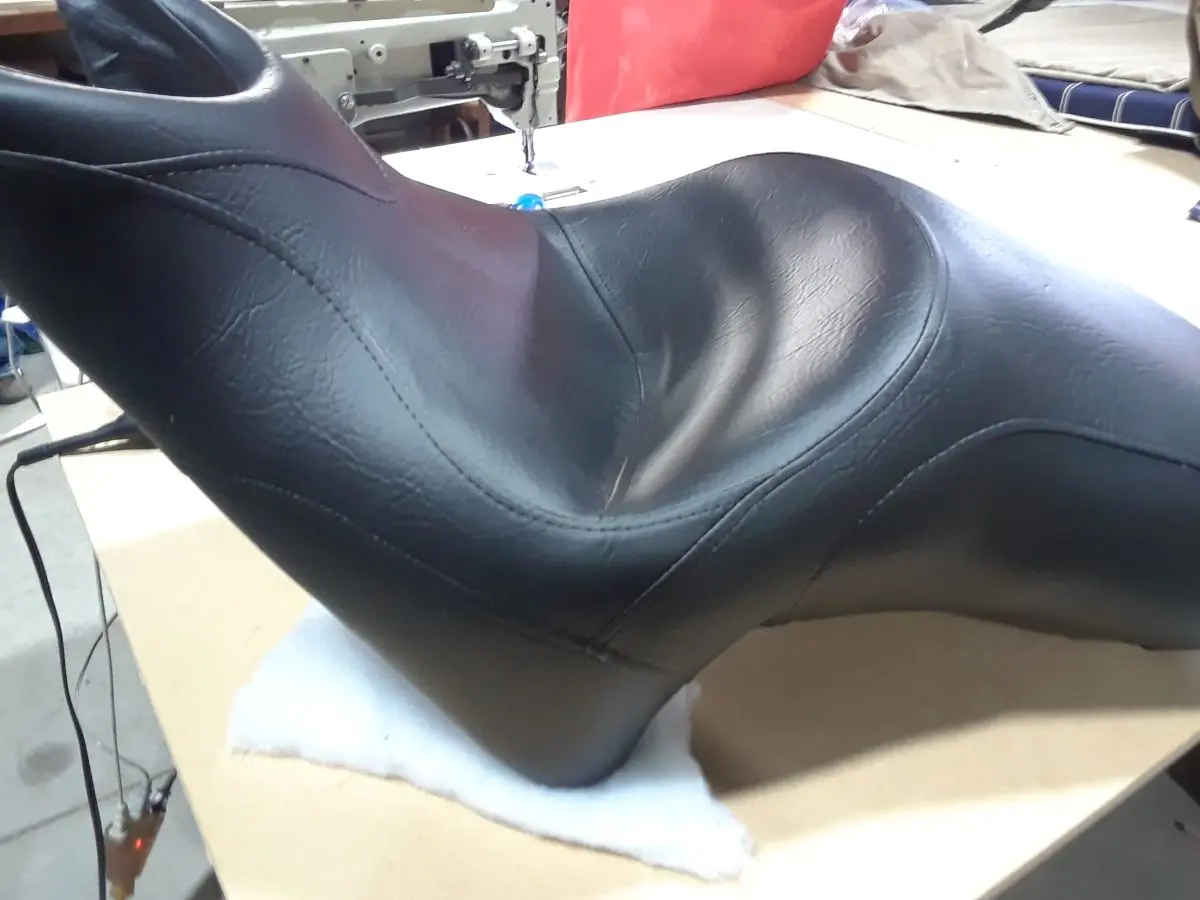 Selle de moto en finition cuir synthétique noir, posée sur une table de confection en atelier