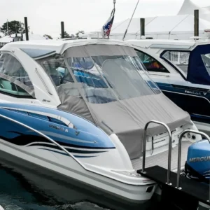 Bateau de luxe bleu et blanc équipé d’une toile grise sur mesure et d’un pare-brise transparent, amarré dans une marina avec moteurs Mercury en arrière-plan.