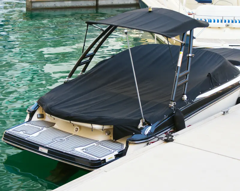 Bateau de plaisance noir avec arche de wake, amarré au quai et recouvert d’une toile noire sur mesure tendue jusqu’à la plateforme arrière.