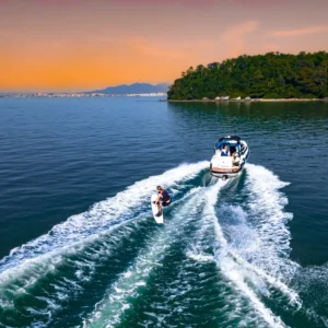 Un bateau de wake sur mesure tracte un surfeur nautique au coucher du soleil, illustrant la pratique du surf de sillage sur plan d’eau calme.