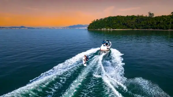 Un bateau de wake sur mesure tracte un surfeur nautique au coucher du soleil, illustrant la pratique du surf de sillage sur plan d’eau calme.