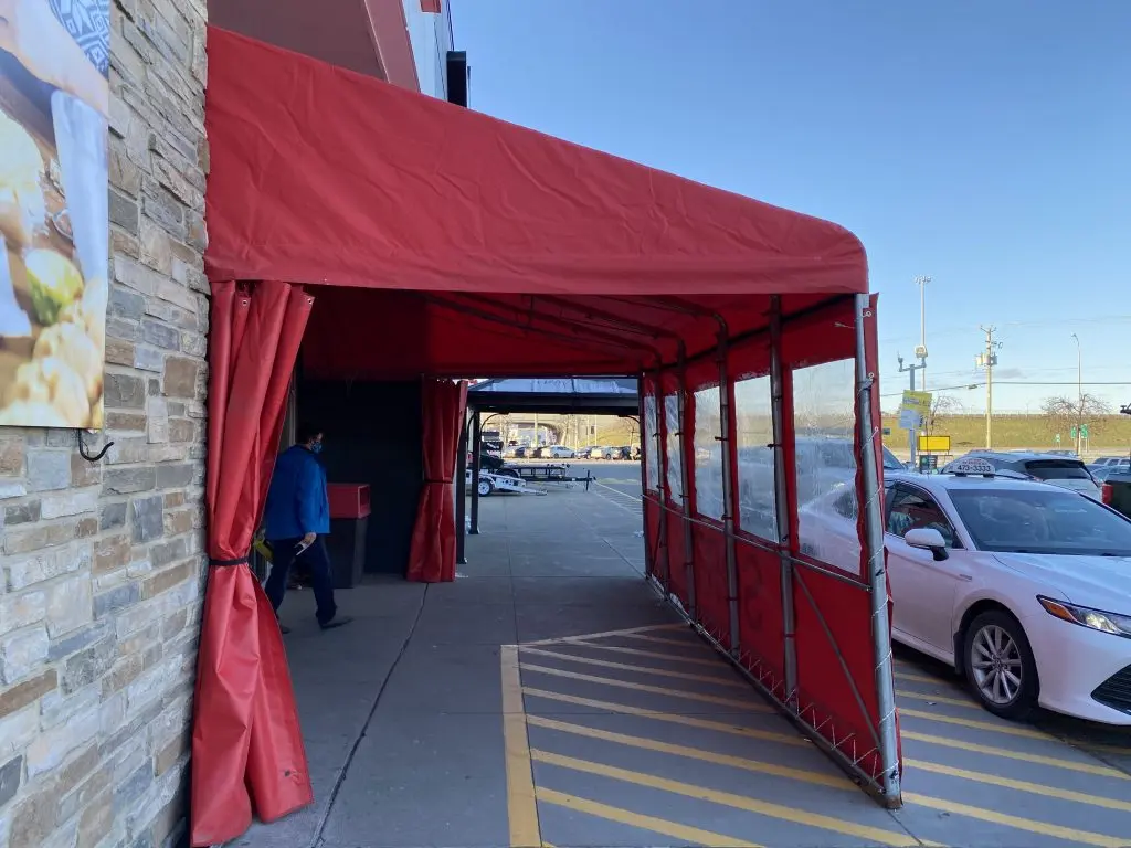 Tunnel d’entrée en toile rouge sur mesure pour commerce, fixé à la façade du bâtiment