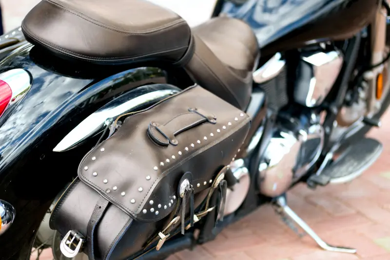 Moto noire équipée d’un siège rembourré et d’une sacoche en cuir avec finition cloutée, vue latérale