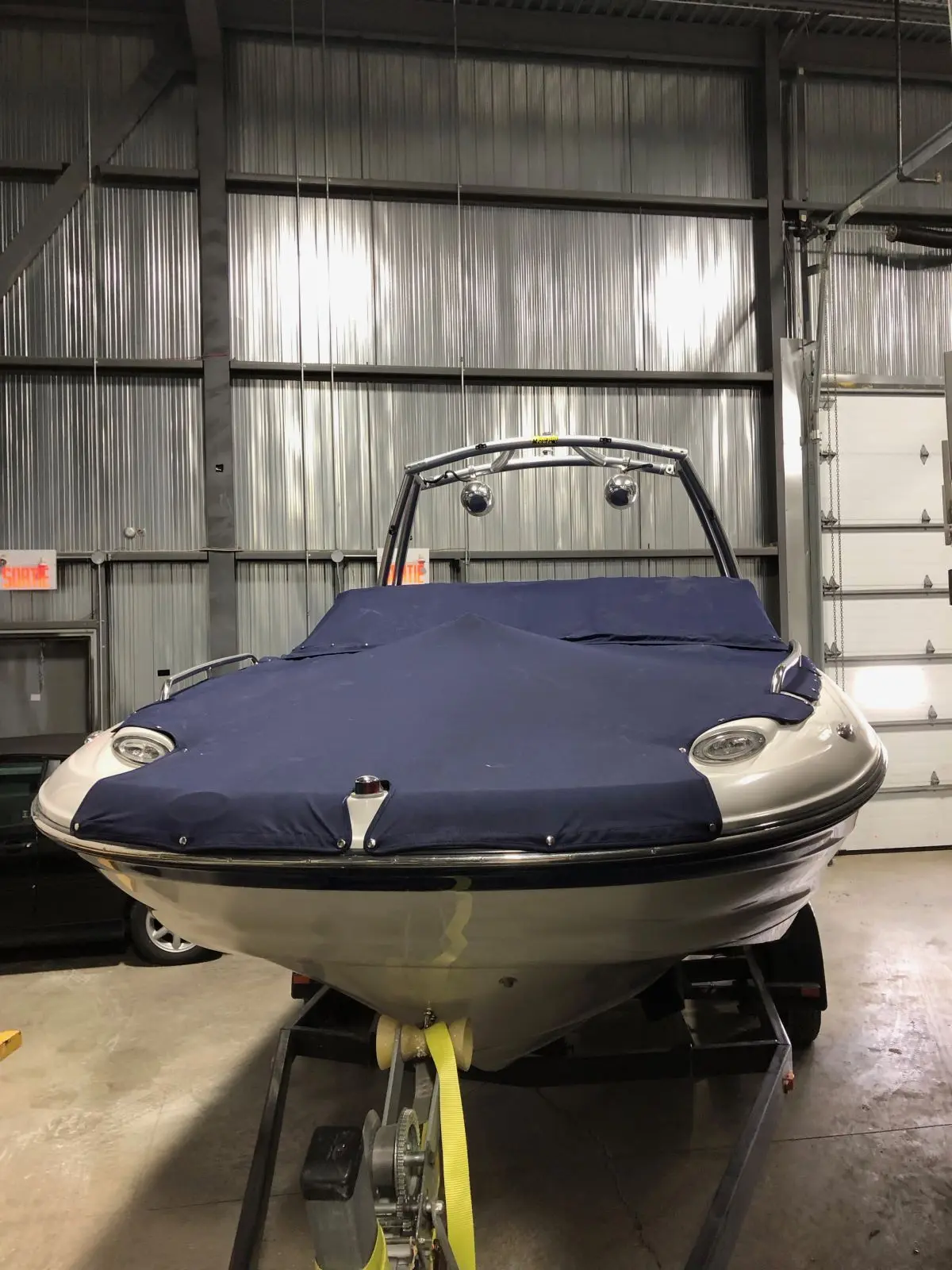 Toile de protection bleue bien ajustée sur un bateau à moteur entreposé à l’intérieur, fixée sur remorque.
