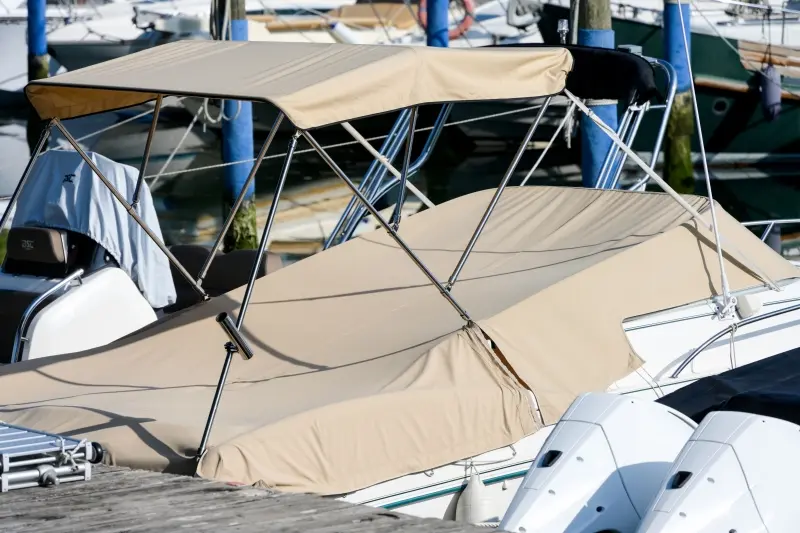 Toile express beige sur mesure installée sur un bateau à moteur amarré à un quai, protection complète contre les intempéries.